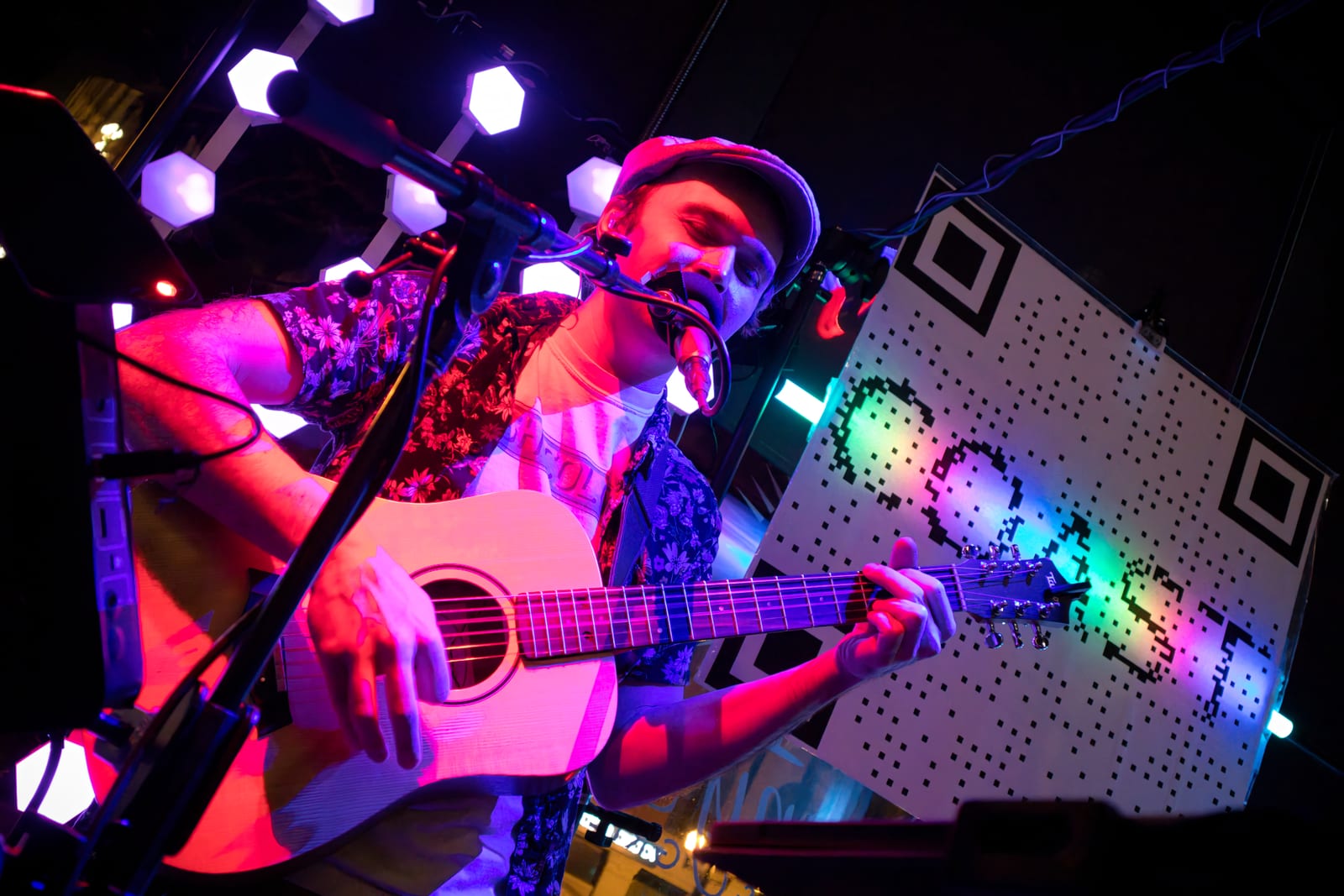 Stephen Michael performing acoustic guitar beneath colorful stage lights